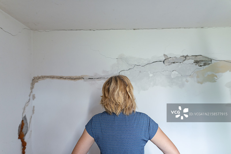 女人查看地震后受损墙壁图片素材