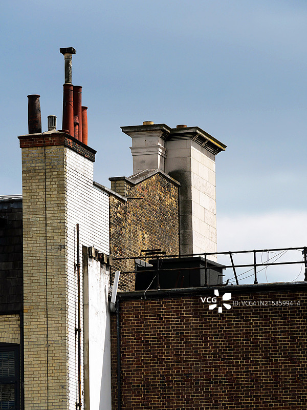 伦敦，英格兰，英国的住宅建筑后墙和山墙特写，墙面为风化的棕色和白色砖块，屋顶上有烟囱。阳光明媚，蓝天映衬，色彩自然。图片素材