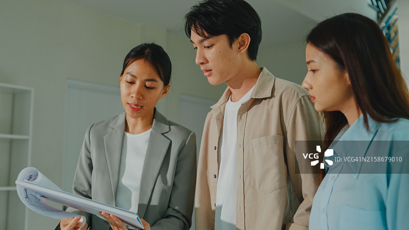 亚洲女房地产经纪人向租户解释并展示新房客厅，房东向幸福的夫妇客户出售房地产图片素材