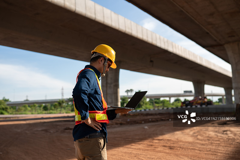 站在桥前看笔记本电脑的建筑工人图片素材