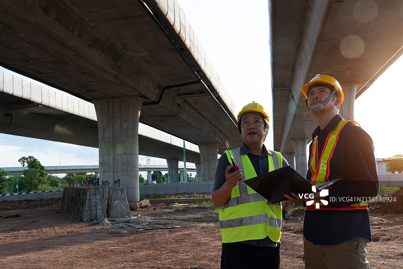 两个男人站在建筑工地上，其中一个拿着写字板图片素材