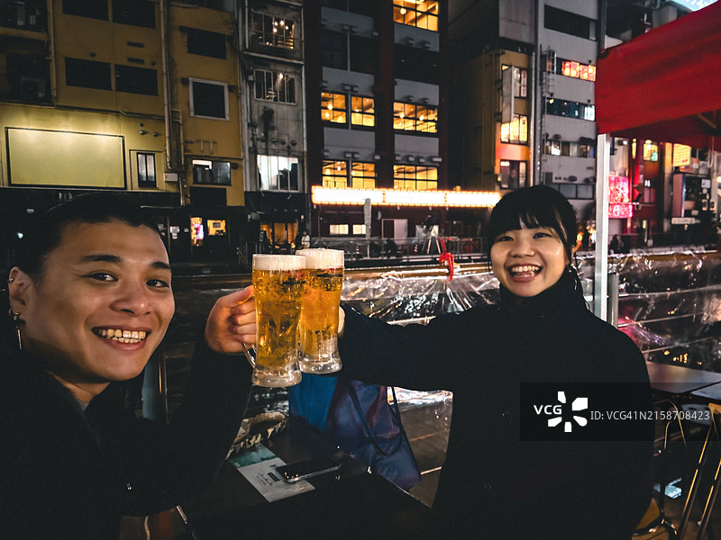 情侣举杯畅饮啤酒，庆祝夜晚外出图片素材