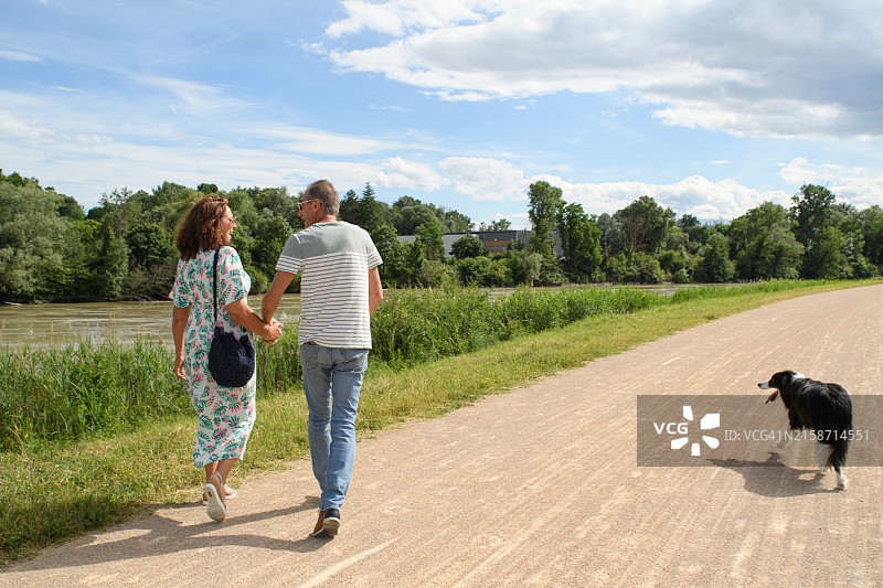 一对老年夫妇带着他们的狗在河边散步图片素材