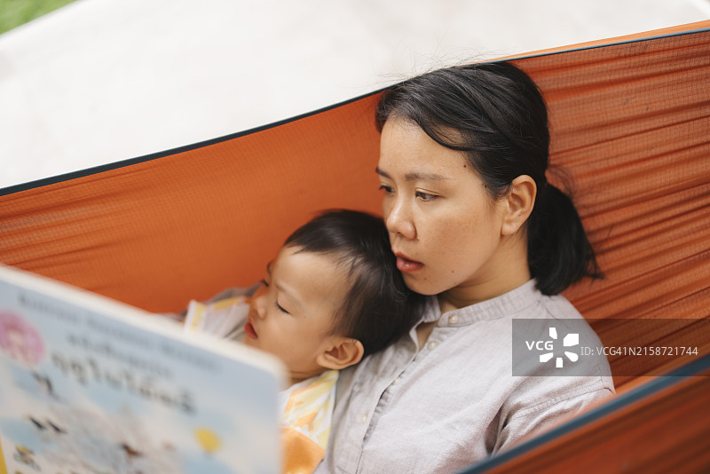 在吊床上给宝宝读书的亚洲年轻母亲图片素材