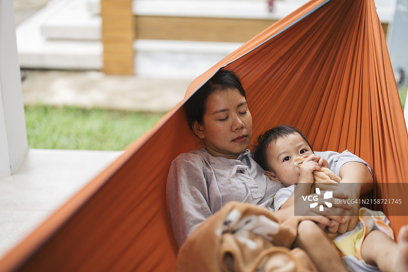 在吊床上给宝宝读书的亚洲年轻母亲图片素材