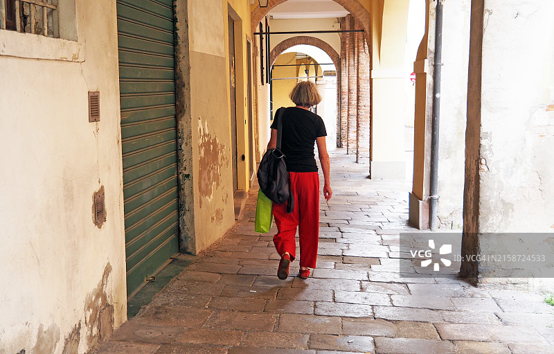 年长妇女在古老的帕多瓦画廊中行走，背影。图片素材
