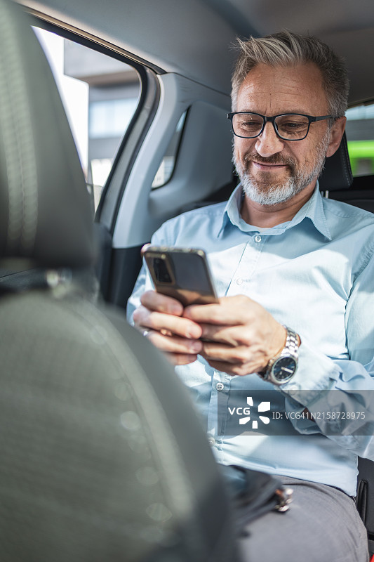 成熟商人乘坐出租车通勤时，远程使用智能手机工作图片素材