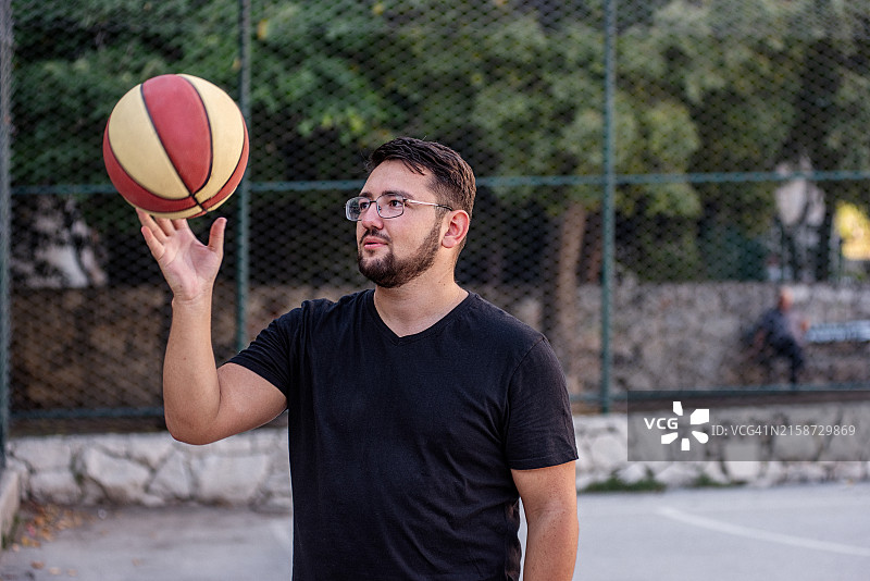 在室外球场上转篮球的年轻男人图片素材