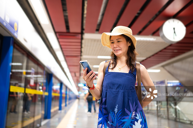 年长的亚洲女游客在曼谷的铁路站台上等候捷运，同时使用智能手机图片素材