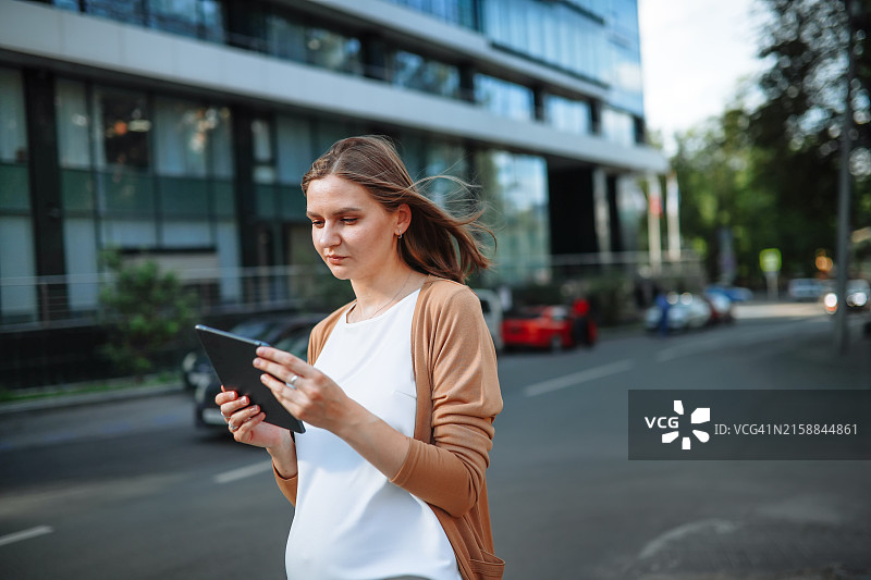 城市办公环境：使用平板电脑和手机的女性，关注科技与投资图片素材