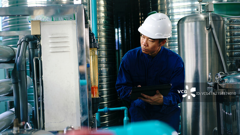 戴安全帽的工程师在水处理厂调节阀门并检查工业管道上的压力表，进行水灌装图片素材