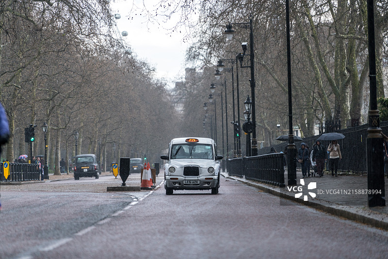典型的传统英式出租车在伦敦林荫路附近雨中行驶图片素材