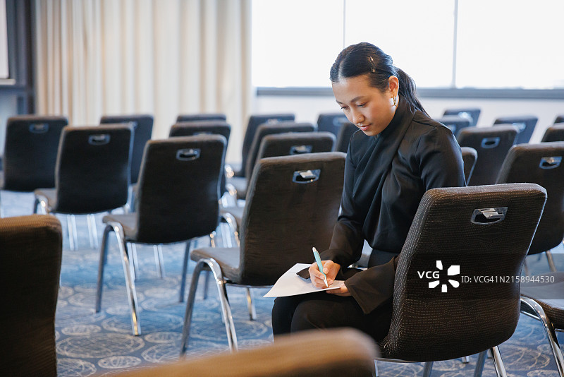 坐在空旷会议室里手持纸笔的亚洲女商人肖像图片素材