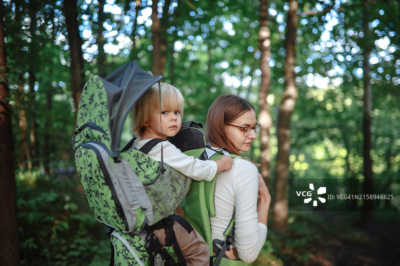 安全徒步：中年母亲和幼儿探索森林，使用专用设备确保儿童户外安全图片素材