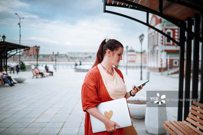 体型偏胖的中年女人在城市河边用笔记本电脑进行户外远程工作和网上购物图片素材