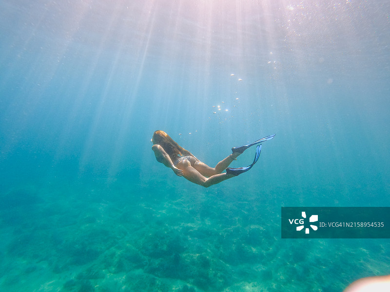 穿着比基尼和脚蹼在海底附近潜水的美丽女人图片素材