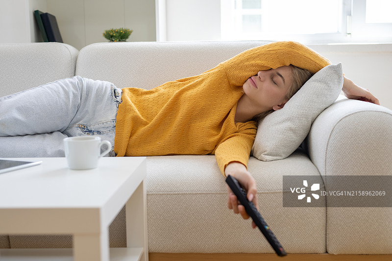 女人在沙发上睡着了，电视遥控器放在一边图片素材
