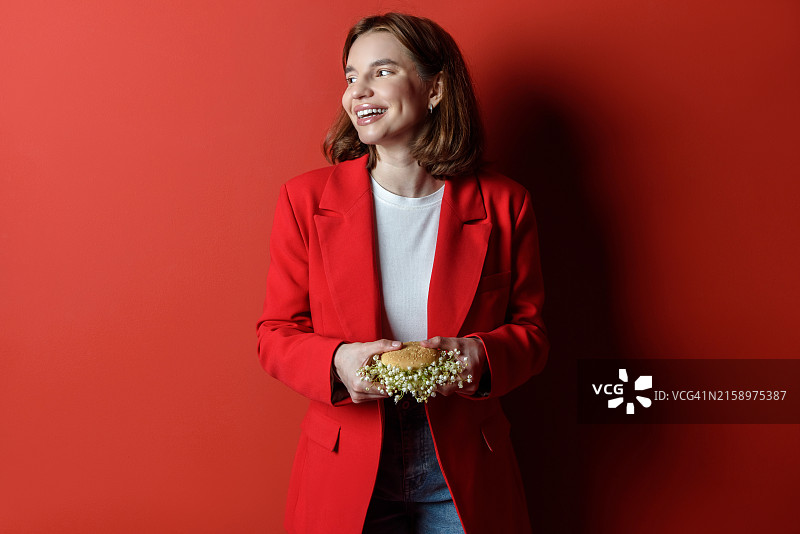 微笑的女人拿着纯素鲜花汉堡，红色背景，健康饮食理念图片素材