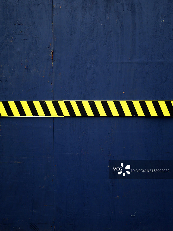 蓝色木板上的黄黑条纹警示牌，纽约曼哈顿建筑工地边界特写，自然光图片素材