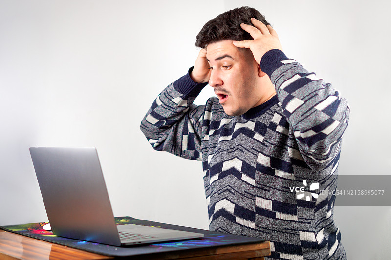 年轻男人手托着头在桌旁使用笔记本电脑图片素材