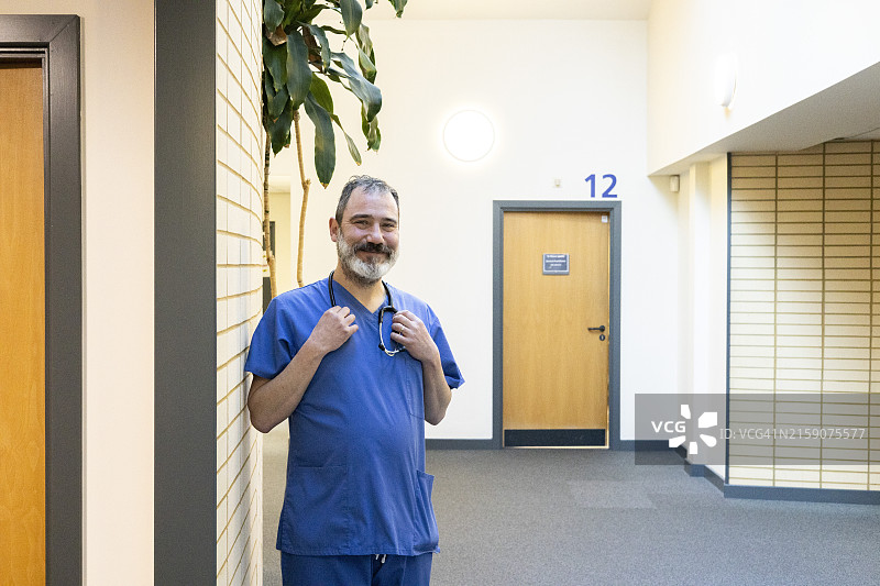 穿着蓝色手术服的男人在医疗诊所的走廊里微笑图片素材