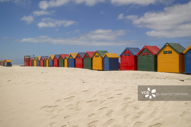 晴朗蓝天下沙滩上的一排彩色海滩小屋图片素材