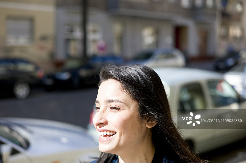 一位微笑的女士在阳光明媚的户外，背景是模糊的街道和停放的汽车图片素材