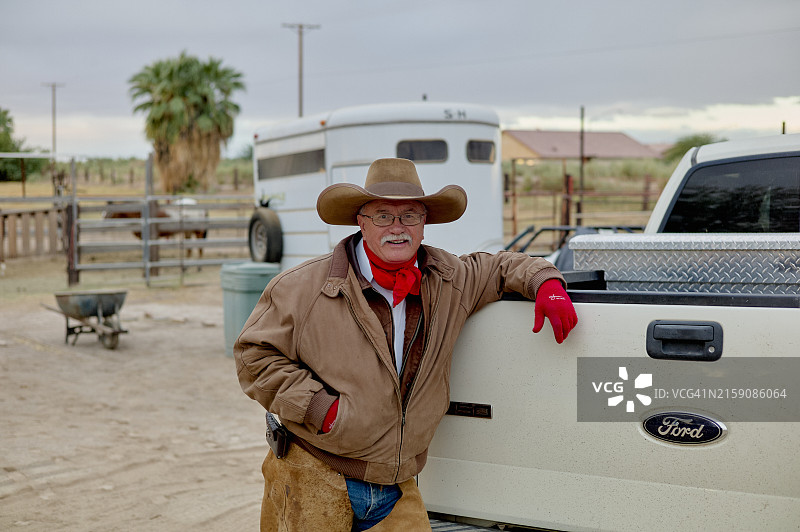 戴牛仔帽和红手套的男子靠在白色福特皮卡上，背景是乡村景色图片素材