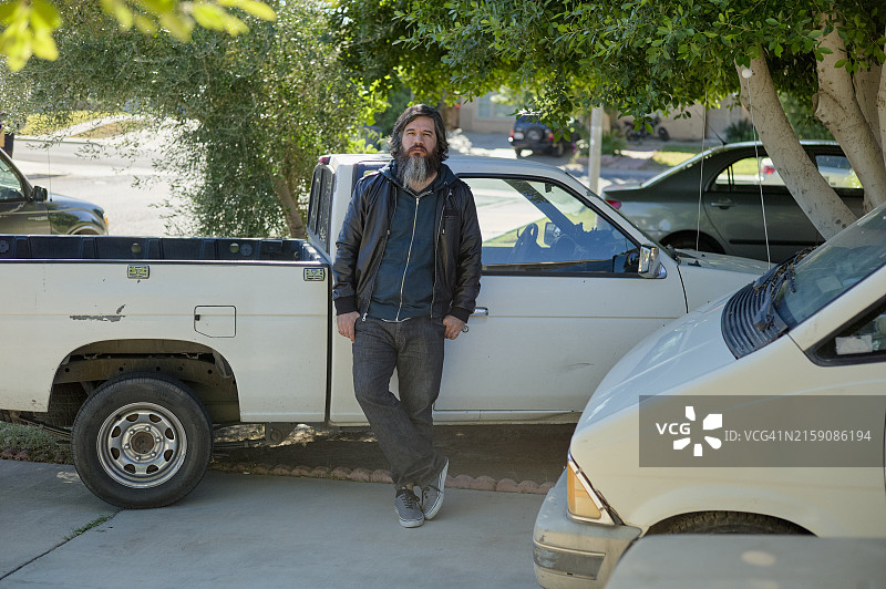 男子站在住宅街道的两辆白色皮卡之间，背景是树木和房屋图片素材