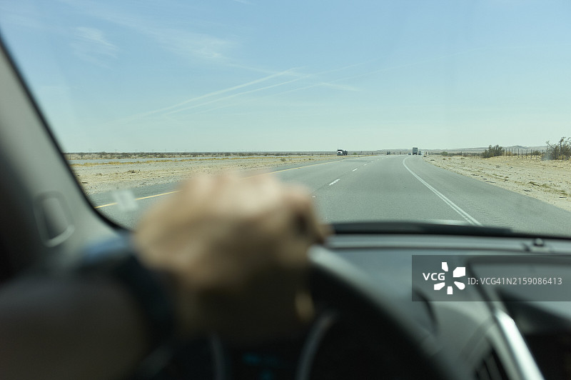 从车内看到的驾驶员手握方向盘，前方是一条笔直的道路和蓝天图片素材