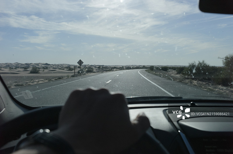 第一人称视角：车辆行驶在沙漠公路上，手握方向盘图片素材