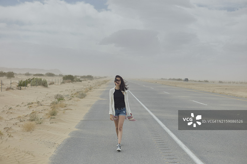 女人走在空旷的沙漠公路中央，天空阴云密布图片素材