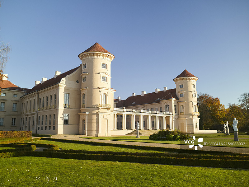 沐浴在阳光下的宏伟历史豪宅，有两座突出的塔楼和对称的建筑，周围环绕着修剪整齐的草坪和一些雕像图片素材