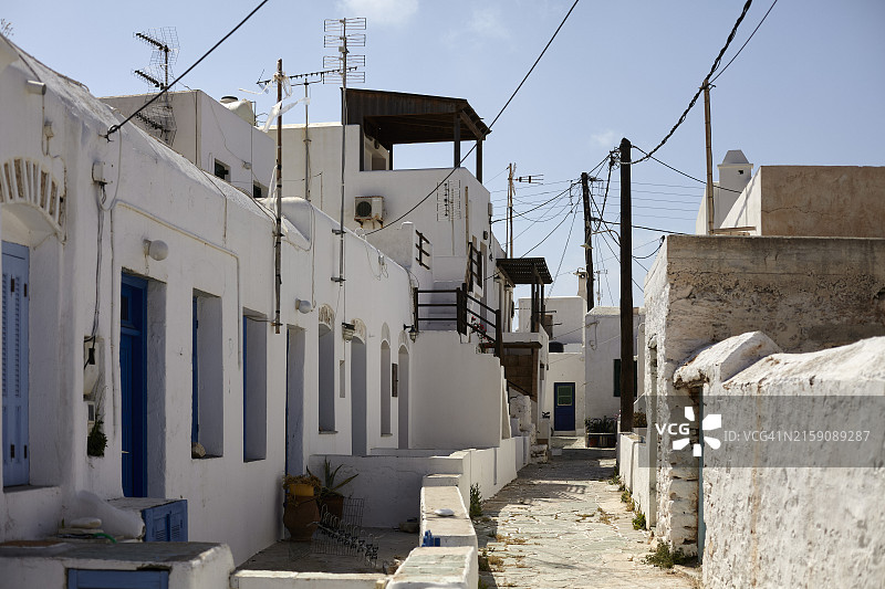 传统地中海村庄里的一条狭窄小巷，白色建筑和蓝色门窗，晴朗的天空下电线纵横交错图片素材