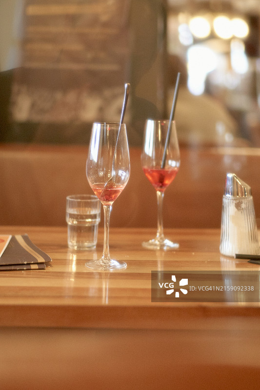 两个酒杯，一个部分装满玫瑰红葡萄酒，放在木制吧台上，旁边放一杯水和一个盐瓶，模糊的背景暗示着舒适的餐厅环境图片素材