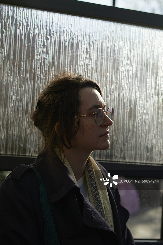 在磨砂玻璃窗背景下，阳光洒在脸上的人图片素材