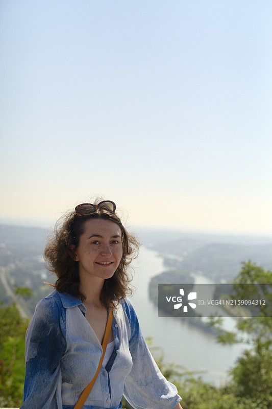 戴着太阳镜，在蜿蜒的河流和茂盛的绿色植物前摆姿势的微笑的女人图片素材