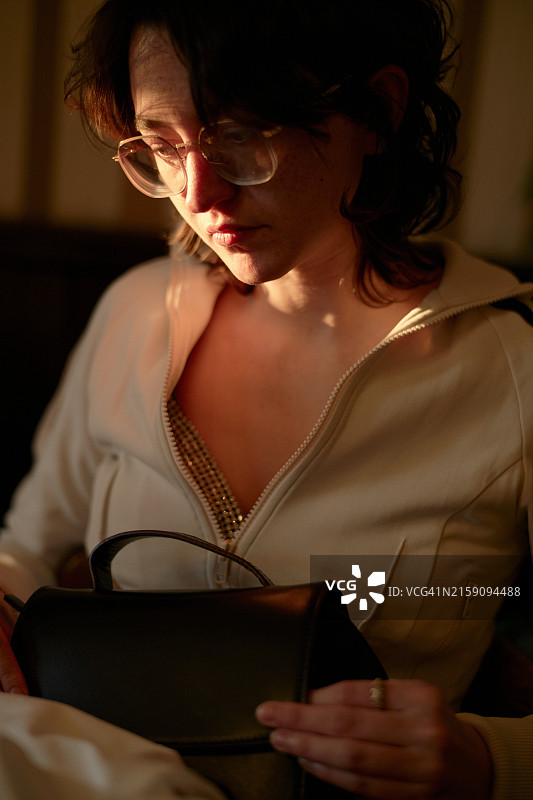 女人在暖光的照耀下看着黑色手提包，突显出她的轮廓图片素材