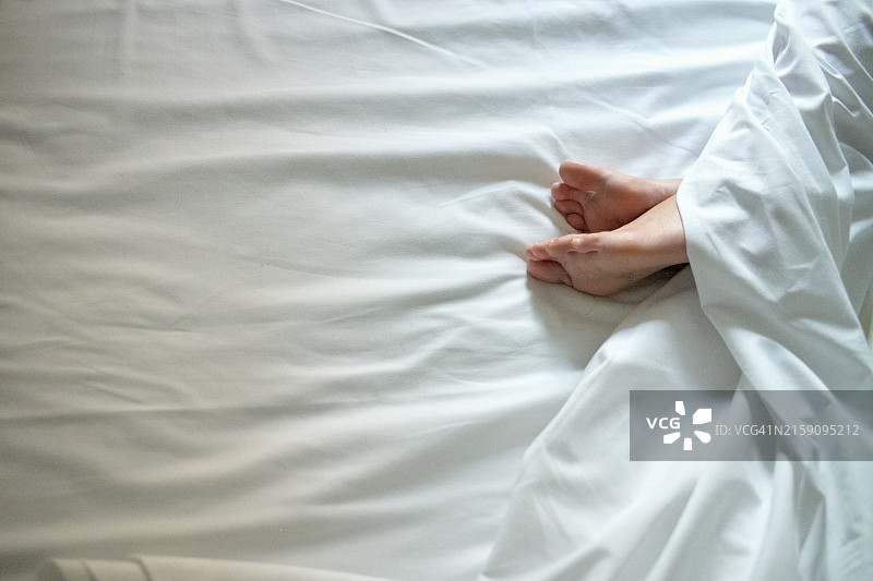 一个人的赤脚从白色床单的白色羽绒被下伸出图片素材