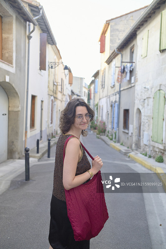 留着齐肩发的年轻女子走在狭窄的街道上，回头微笑图片素材