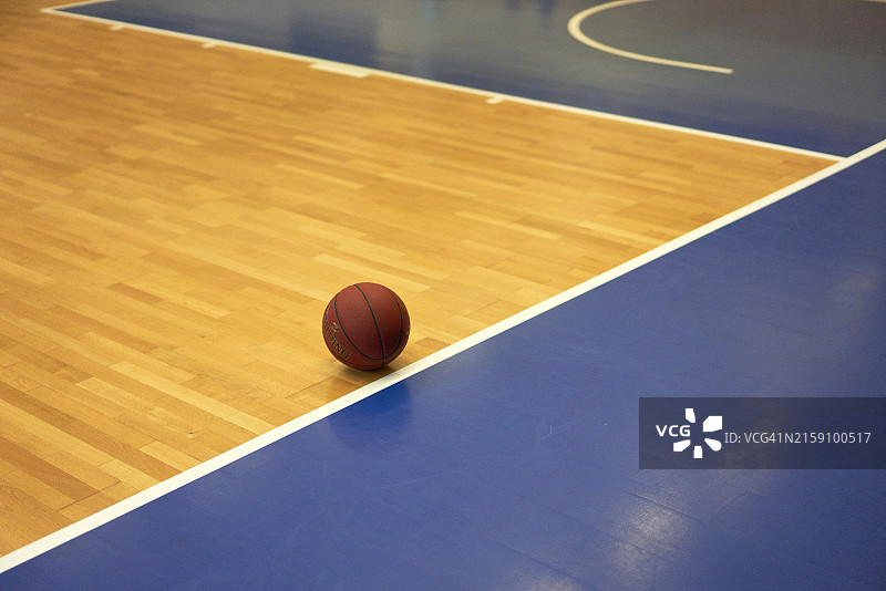篮球静置在带有蓝色边界的光滑木质球场上图片素材