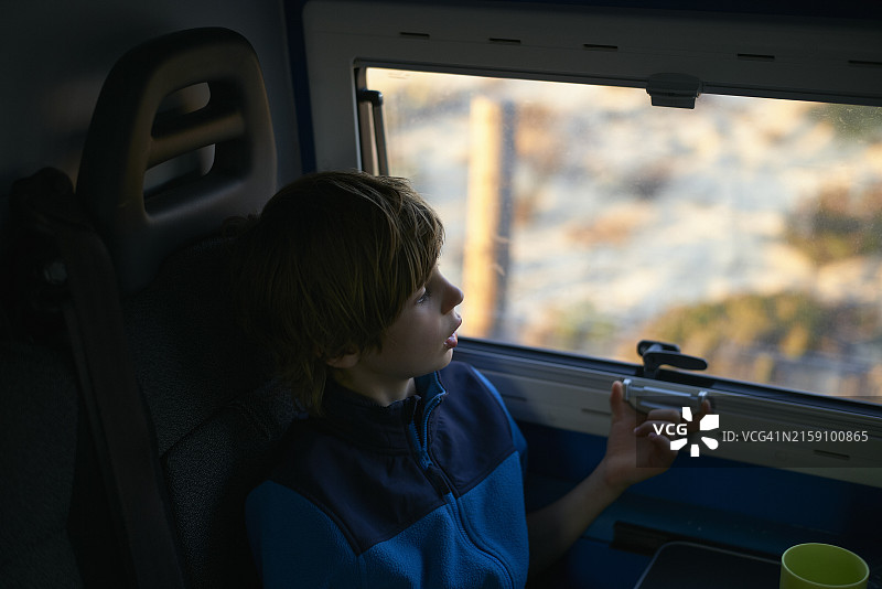 一个年轻人拿着智能手机若有所思地望着火车窗外，背景是模糊的户外风景图片素材