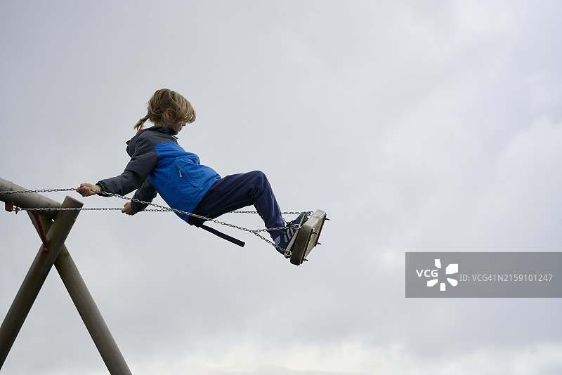 在多云天空下享受高空秋千的蓝色外套儿童图片素材