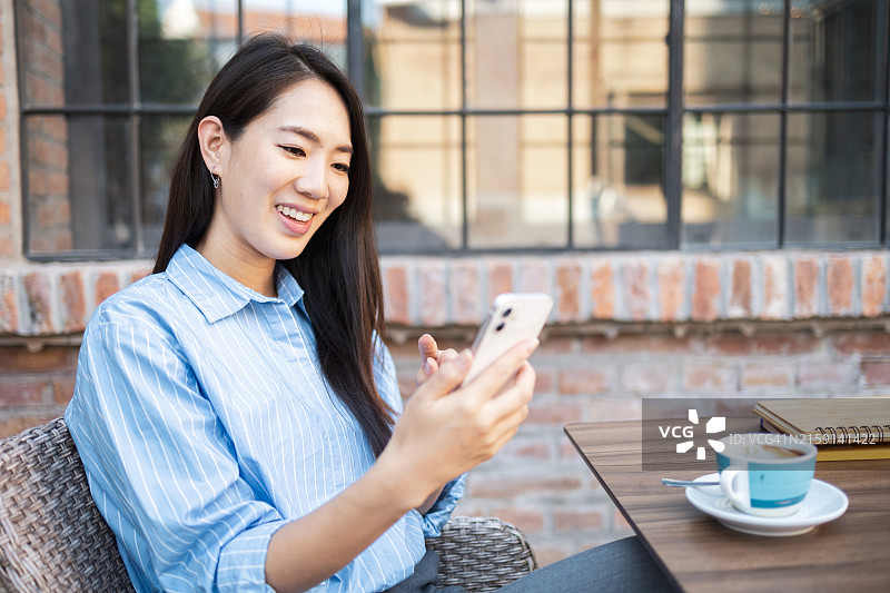 在户外咖啡馆使用智能手机微笑的亚洲女人图片素材