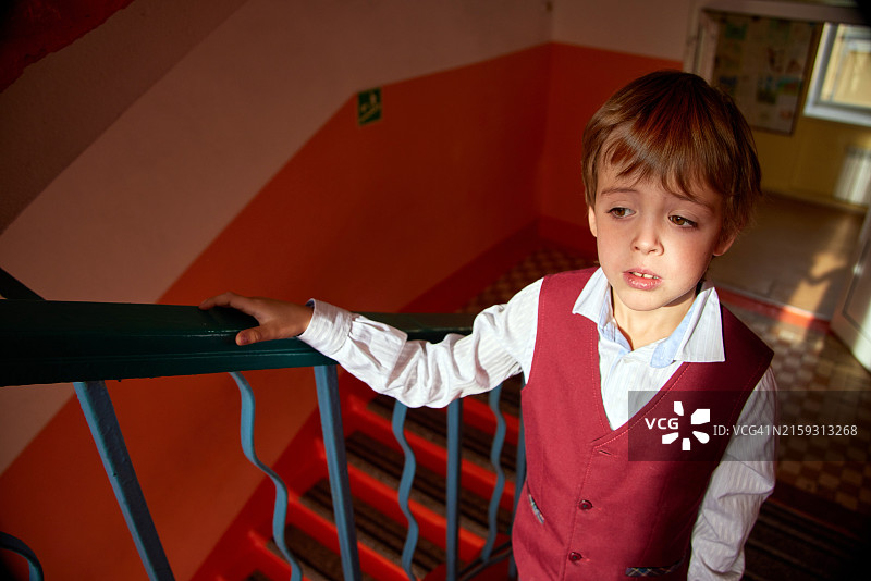 阳光照耀下，身穿校服站在楼梯上的沉思小男孩图片素材