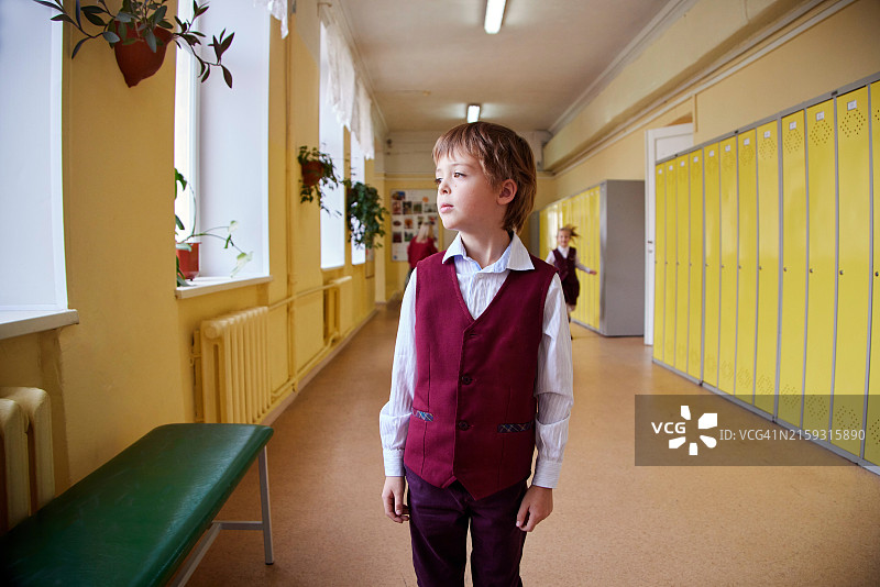 穿着校服的男孩走在教育机构的走廊里，可以看到长椅和窗户图片素材
