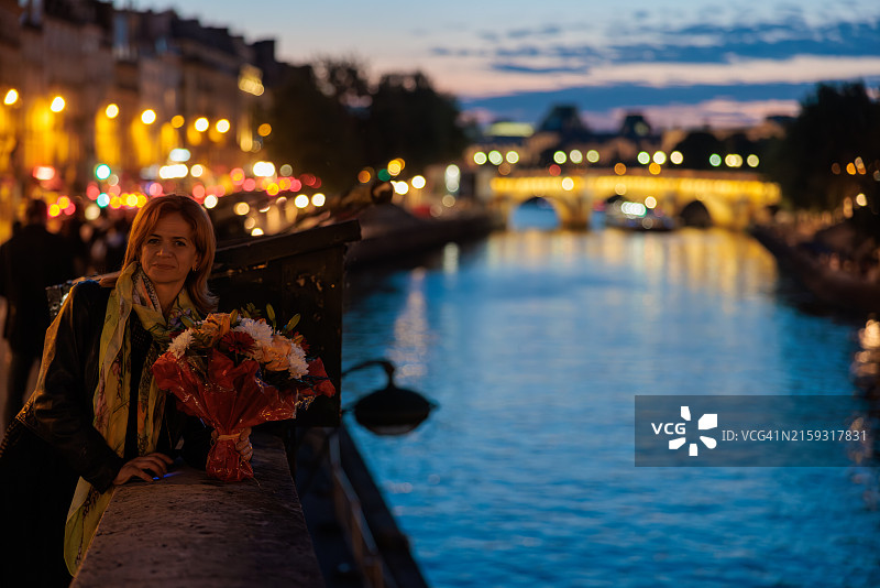 中年妇女在巴黎黄昏的河边拿着一束鲜花对着镜头微笑图片素材