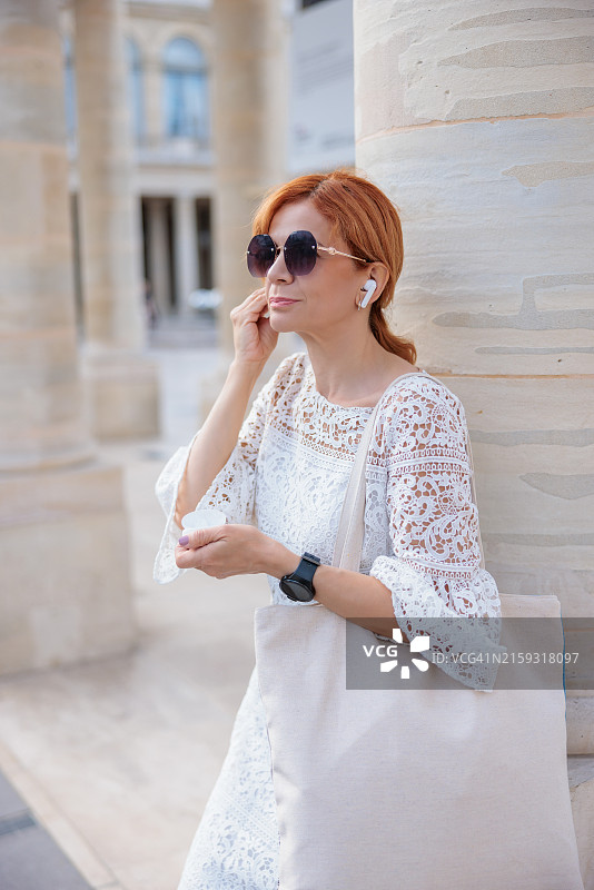 在巴黎的圆柱旁佩戴入耳式耳机的中年女人图片素材