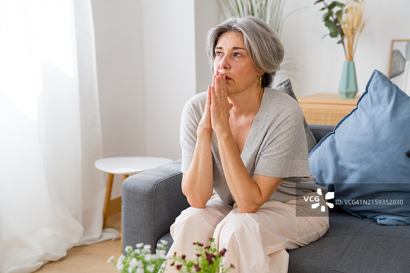 忧虑的老年妇女在沙发上祈祷图片素材
