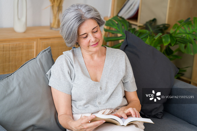 年长的女人在家里的沙发上看书图片素材